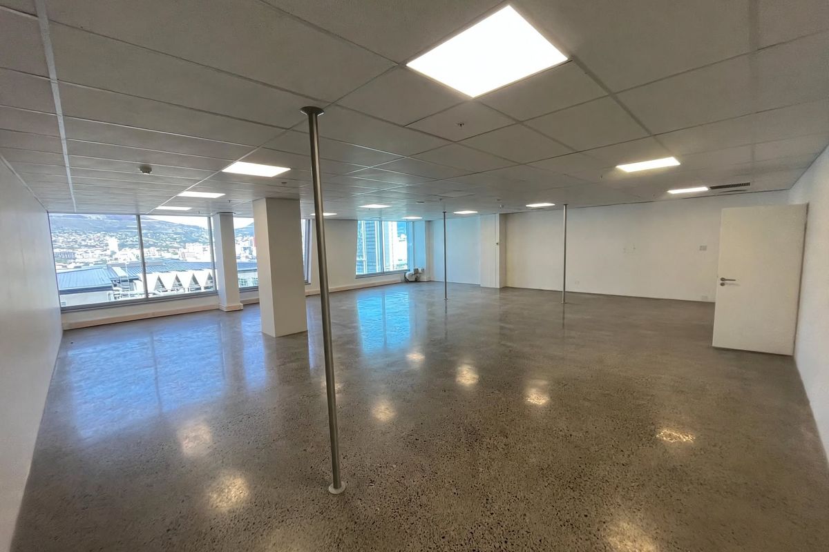 Spacious open-plan office area featuring polished concrete floors, suspended ceilings with recessed lighting, and expansive windows offering natural light and city views.