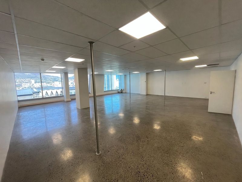 Spacious open-plan office area featuring polished concrete floors, suspended ceilings with recessed lighting, and expansive windows offering natural light and city views.