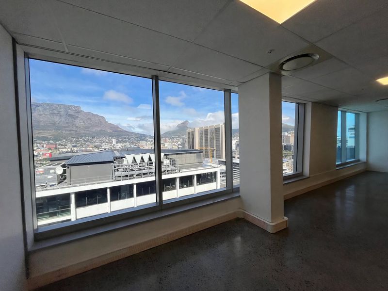Spacious empty office suite featuring polished concrete floors, suspended ceilings, and expansive floor-to-ceiling windows offering panoramic city and mountain views.