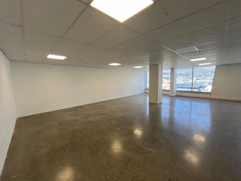 Spacious, open-plan office area featuring polished concrete floors, a modern suspended ceiling with recessed lighting, and expansive windows offering natural light and city views.