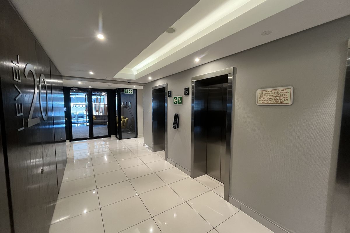 Modern office building elevator lobby featuring polished ceramic floor tiles, recessed ceiling lighting, and stainless steel elevator access points.
