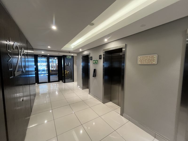 Modern office building elevator lobby featuring polished ceramic floor tiles, recessed ceiling lighting, and stainless steel elevator access points.