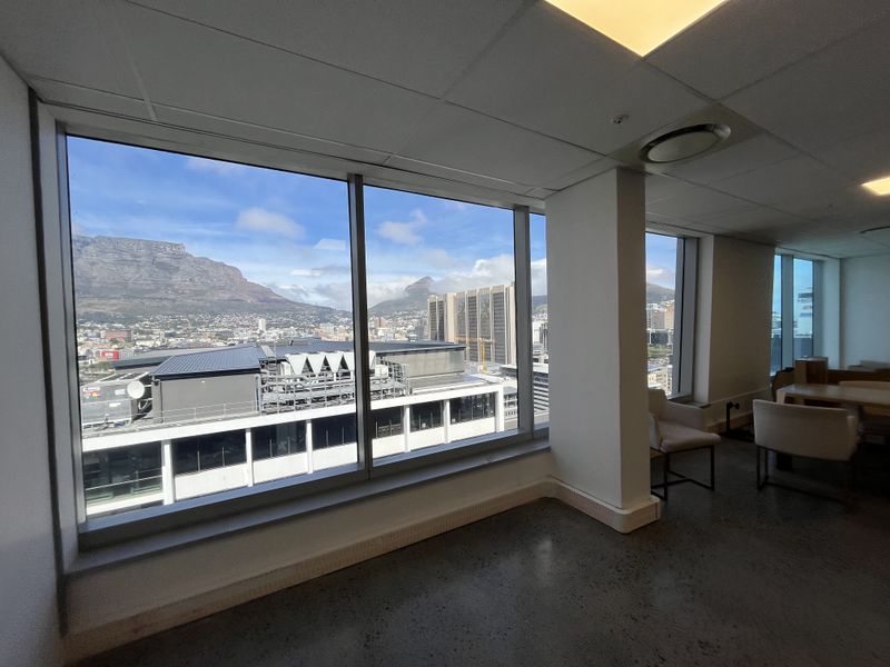 Modern office space featuring polished concrete floors, suspended ceilings, and expansive floor-to-ceiling windows offering panoramic mountain and city views.
