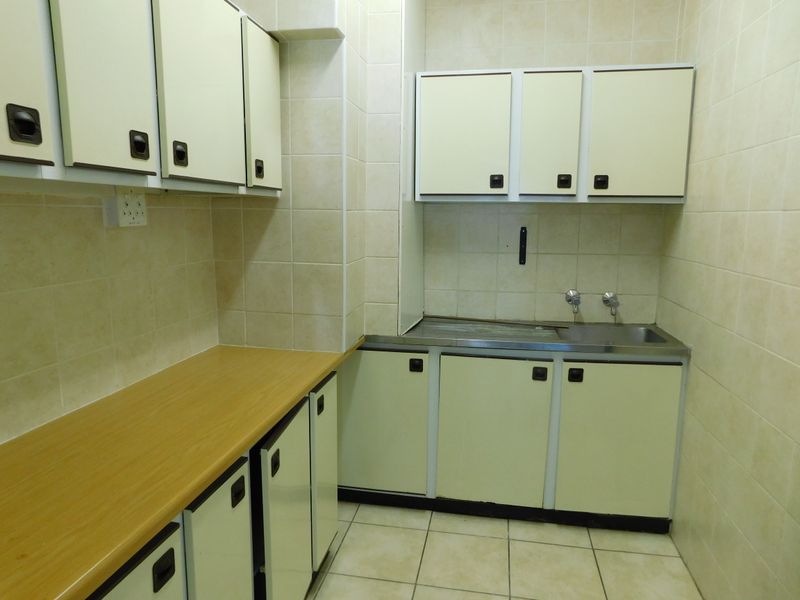 A functional scullery or kitchenette area featuring built-in cabinetry, a stainless steel sink, and tiled finishes throughout.