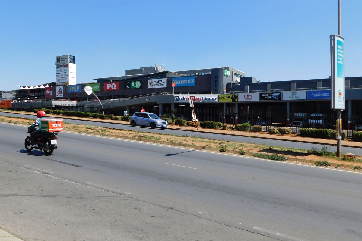 Street-level view of a commercial office and retail center featuring multiple storefronts and prominent signage along a main road.