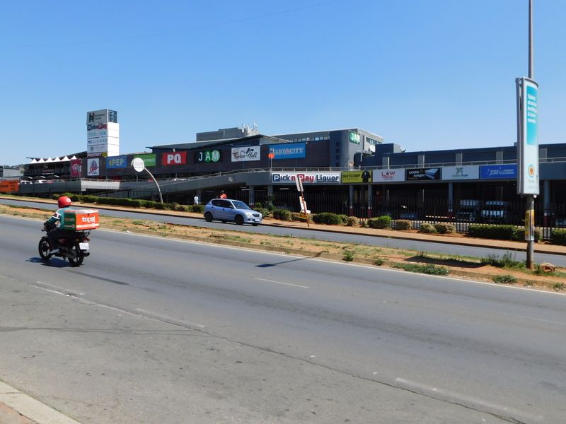 Street-level view of a commercial office and retail center featuring multiple storefronts and prominent signage along a main road.