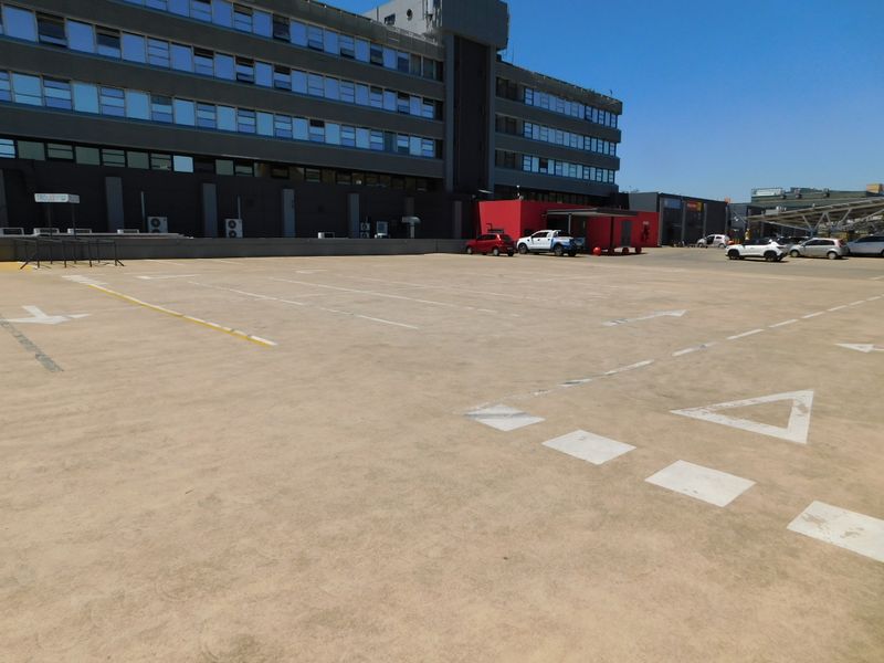 A large paved outdoor parking area adjacent to a multi-story office building with clearly marked parking bays.