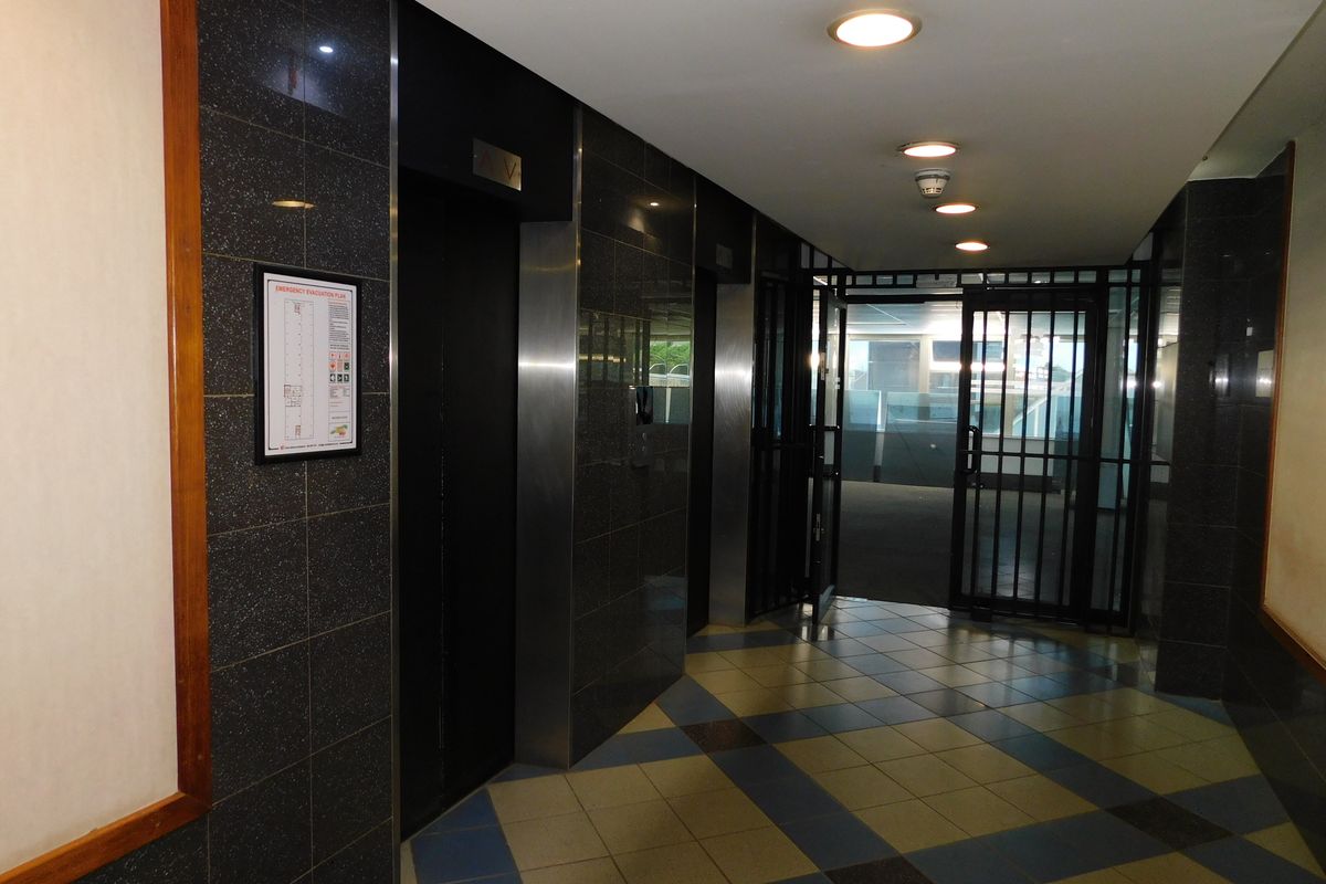 A professional office building hallway featuring granite wall cladding, tiled flooring, recessed lighting, and elevator access with a secure entrance gate.