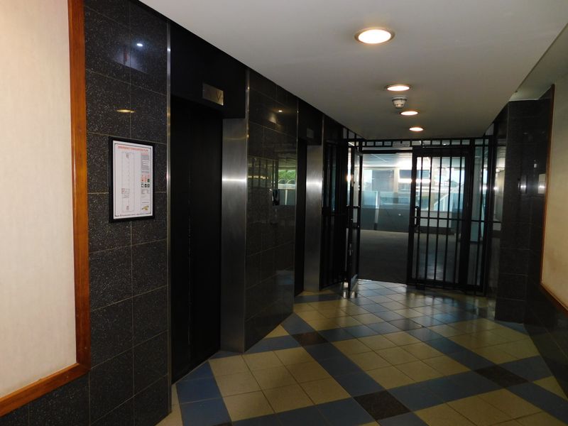 A professional office building hallway featuring granite wall cladding, tiled flooring, recessed lighting, and elevator access with a secure entrance gate.