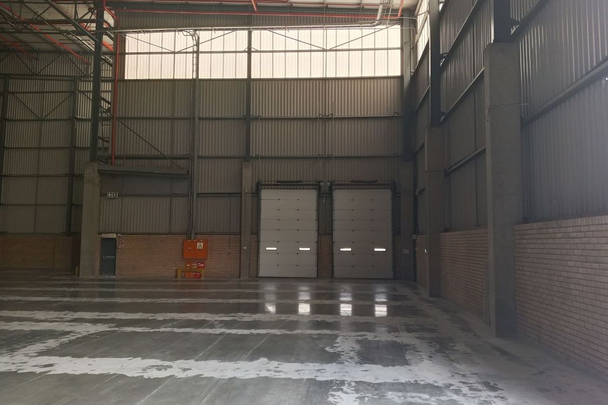 Spacious industrial warehouse featuring high ceilings, exposed steel structure, concrete flooring, and dual roller shutter doors for efficient loading access.