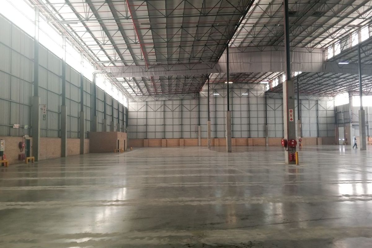 Spacious industrial warehouse featuring high ceilings with exposed steel trusses, polished concrete flooring, and metal wall cladding, equipped with fire safety infrastructure.