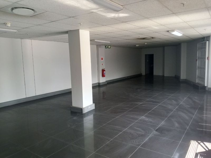 A spacious, empty industrial open-plan area featuring polished dark tiled flooring, a suspended ceiling, and integrated fire safety equipment.