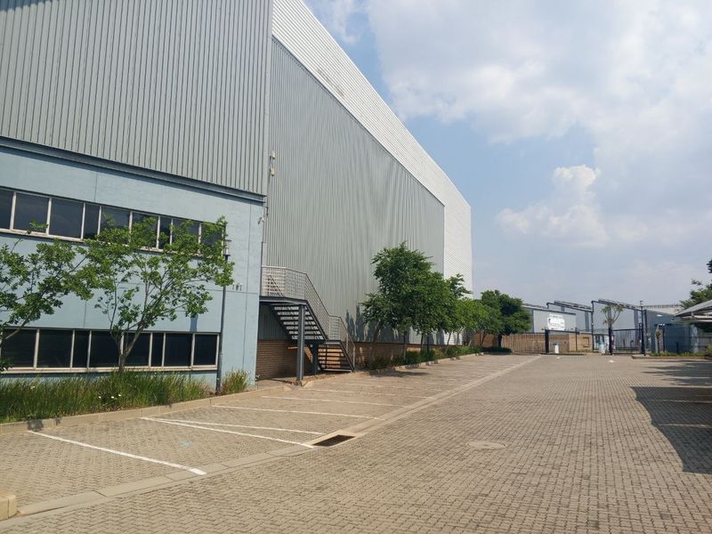 Exterior view of an industrial warehouse facility featuring metal cladding, an external staircase, and a paved parking area.