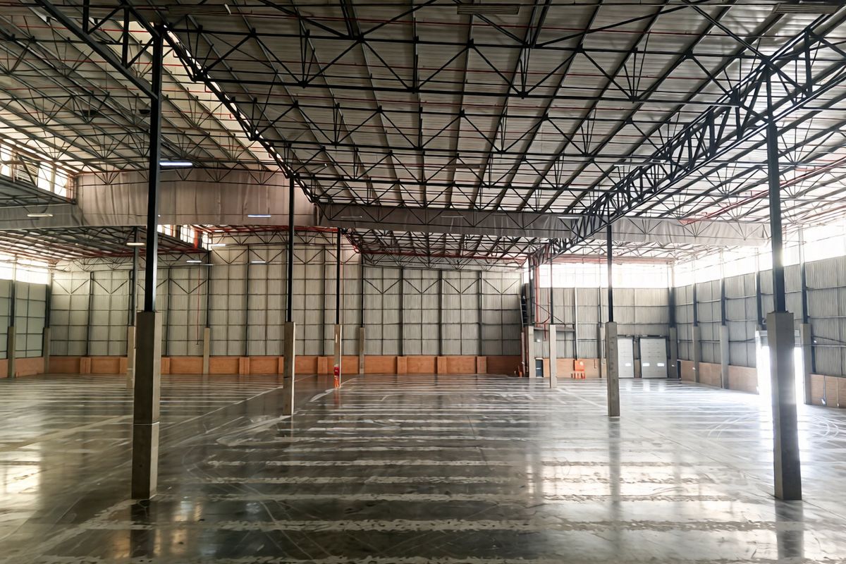 A spacious, open-plan industrial warehouse featuring high-clearance steel truss roofing, polished concrete floors, and large roller shutter access doors.