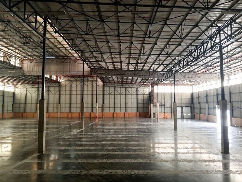 A spacious, open-plan industrial warehouse featuring high-clearance steel truss roofing, polished concrete floors, and large roller shutter access doors.