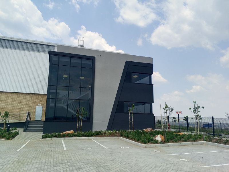 Modern industrial office facade featuring contemporary architectural design, large glass curtain wall, paved parking area, and well-maintained landscaped garden beds.