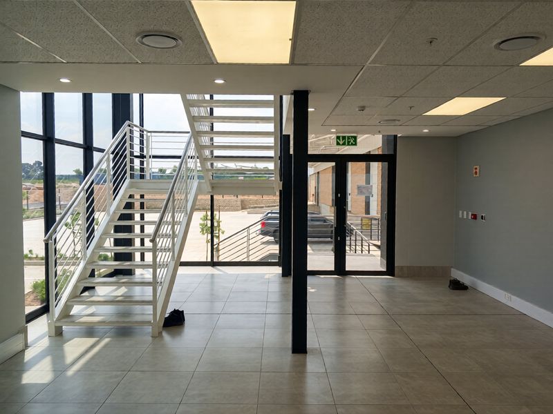 Modern industrial entrance lobby featuring a sleek metal staircase, expansive glass curtain walling, and high-quality ceramic floor tiles in a bright, open-plan space.