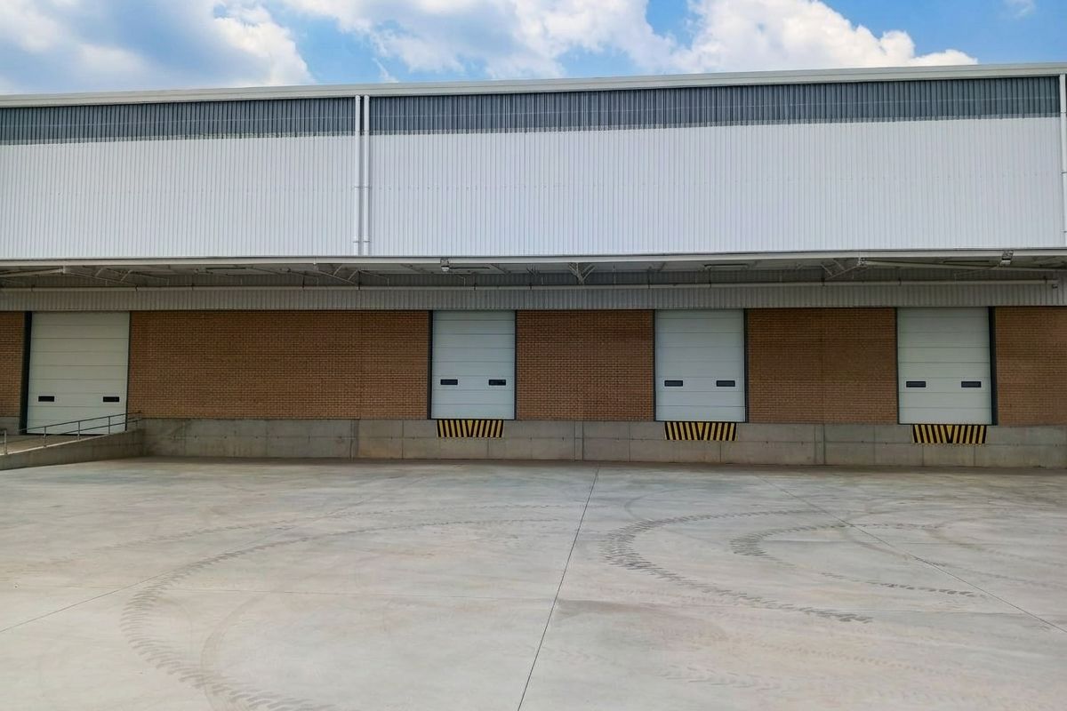 Industrial warehouse exterior featuring multiple roller shutter loading doors, a spacious concrete loading apron, and durable brick and metal cladding construction.