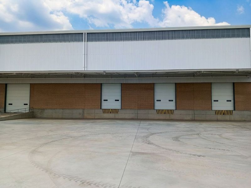 Industrial warehouse exterior featuring multiple roller shutter loading doors, a spacious concrete loading apron, and durable brick and metal cladding construction.