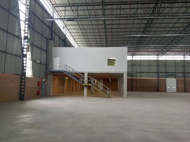 Spacious industrial warehouse featuring a mezzanine level, concrete flooring, exposed steel roof trusses, and a large roller shutter door for efficient access.