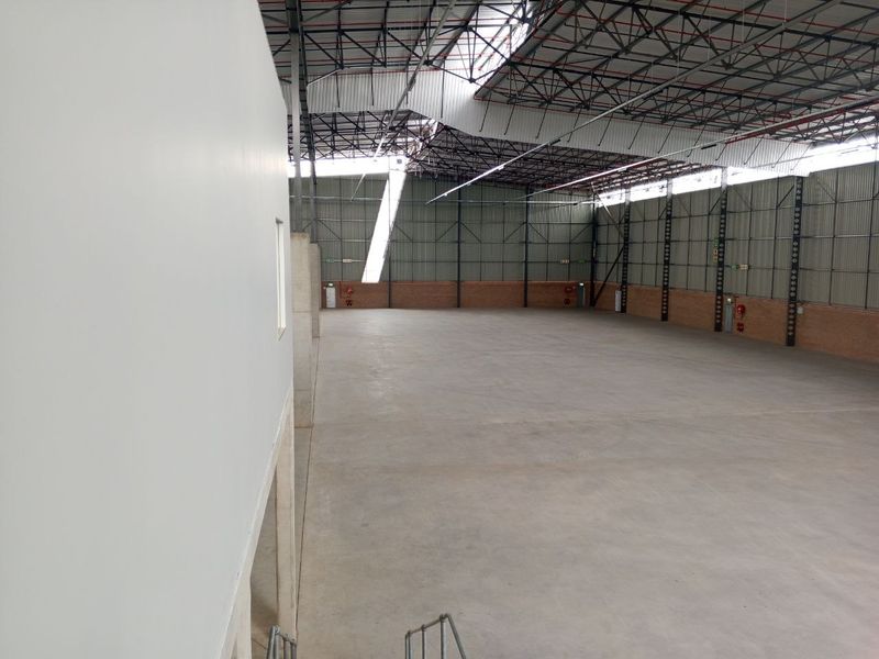 Spacious industrial warehouse unit featuring high ceilings with exposed steel trusses, concrete flooring, and metal wall cladding with integrated fire safety equipment.