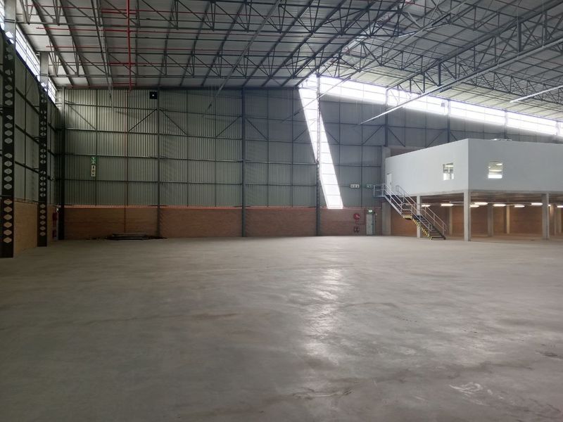Spacious industrial warehouse featuring high ceilings with exposed steel trusses, polished concrete flooring, a mezzanine level with staircase, and ample natural light.