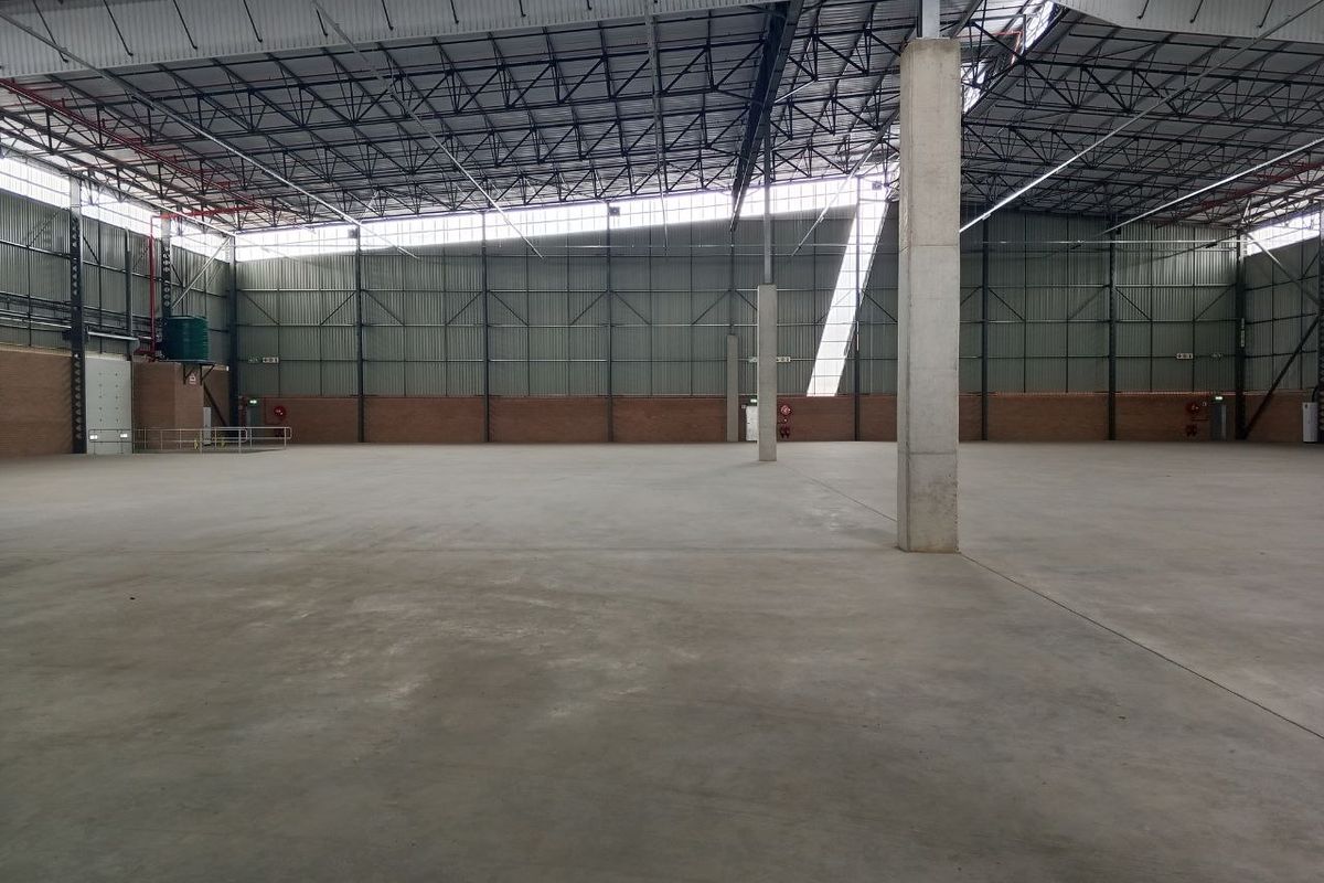 Spacious industrial warehouse interior featuring high ceilings, exposed steel trusses, concrete flooring, and large clerestory windows providing ample natural light.