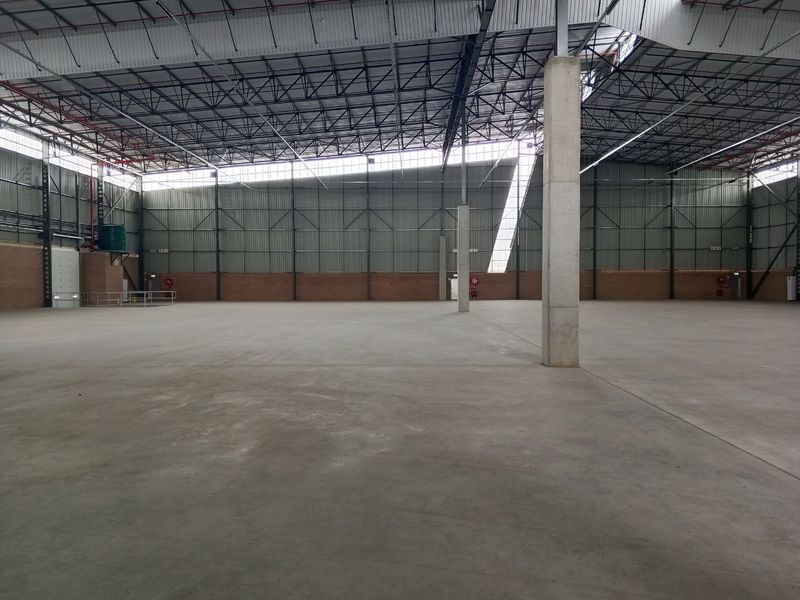 Spacious industrial warehouse interior featuring high ceilings, exposed steel trusses, concrete flooring, and large clerestory windows providing ample natural light.