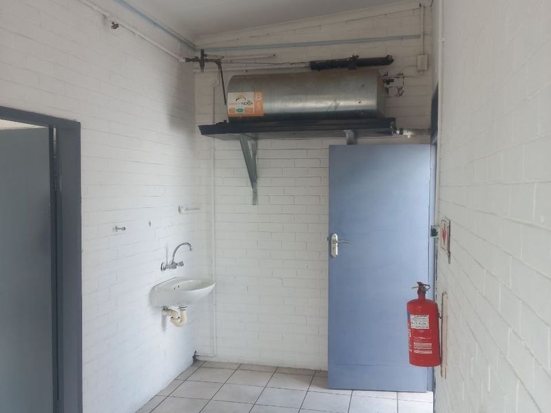 Functional utility space featuring a wall-mounted basin, electric geyser, and tiled flooring, suitable for industrial or service use.
