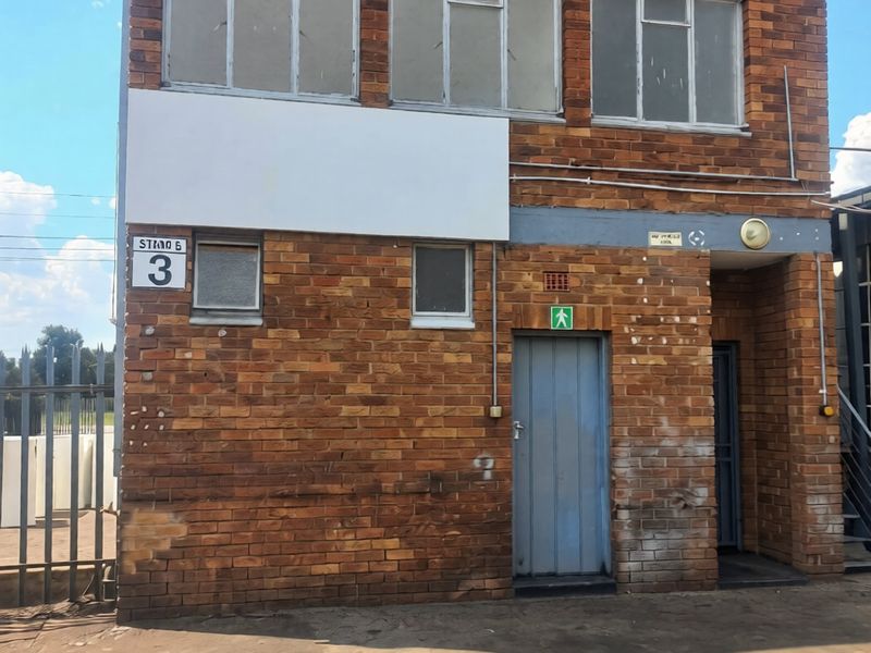 Industrial building facade featuring exposed brickwork, metal-framed windows, and a secure entrance door, showing signs of age and weathering.