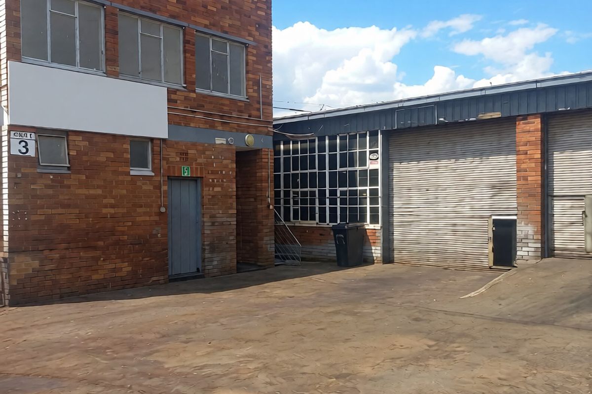 Industrial property exterior featuring brick facade, roller shutter doors, and a spacious concrete yard area suitable for logistics or manufacturing operations.
