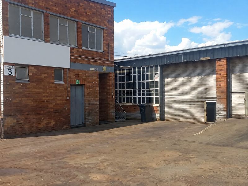 Industrial property exterior featuring brick facade, roller shutter doors, and a spacious concrete yard area suitable for logistics or manufacturing operations.