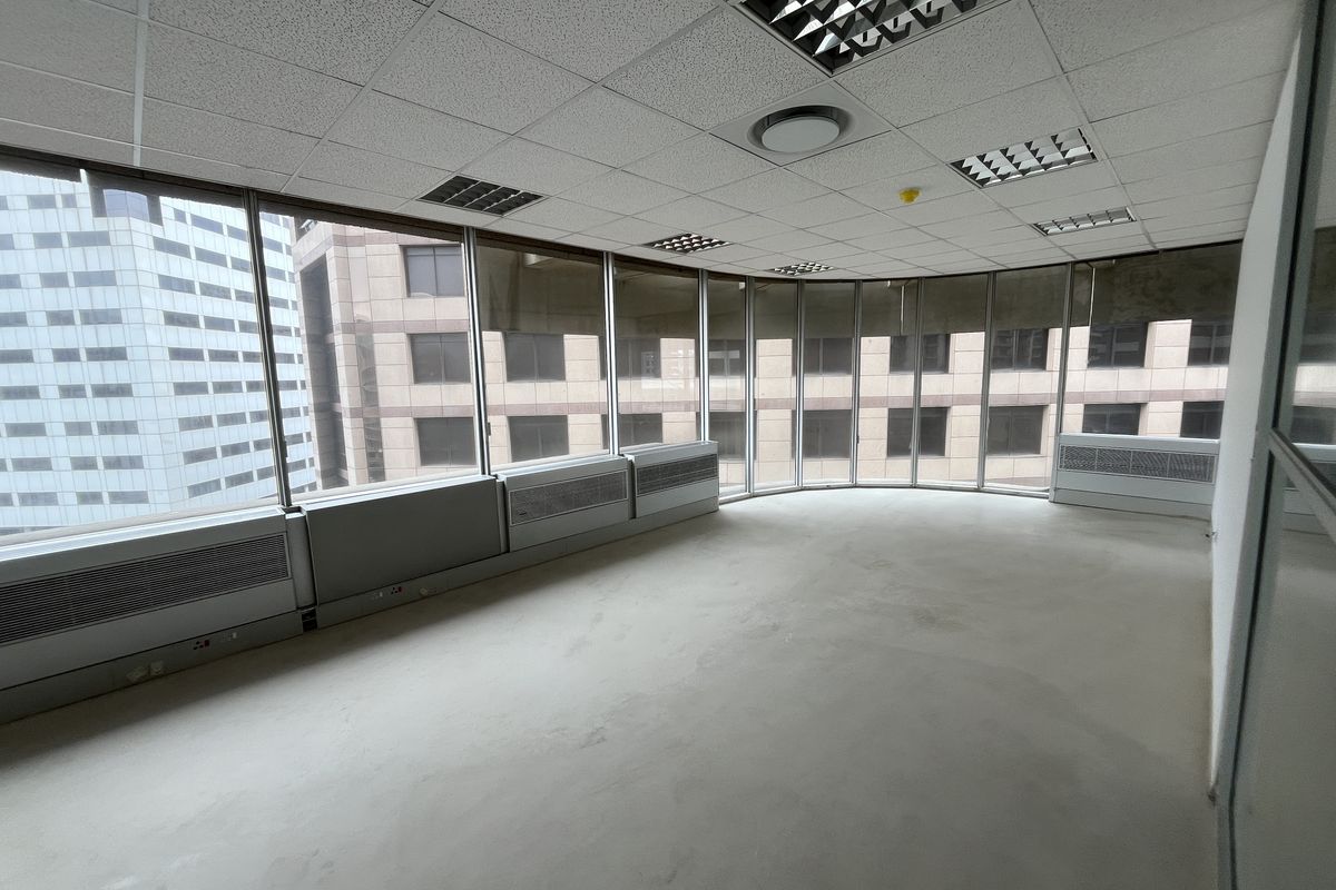 An empty, open-plan office space featuring large floor-to-ceiling windows, suspended ceilings with recessed lighting, and integrated HVAC units.