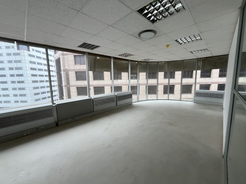 An empty, open-plan office space featuring large floor-to-ceiling windows, suspended ceilings with recessed lighting, and integrated HVAC units.