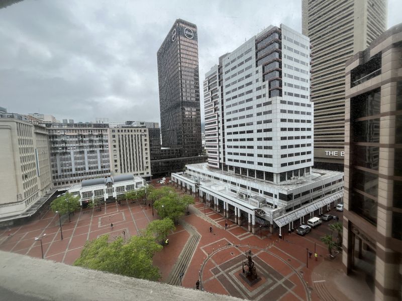 An elevated urban view overlooking a paved city plaza surrounded by high-rise commercial office buildings.