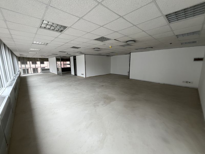 A spacious, open-plan office area featuring a suspended ceiling, recessed lighting, and large windows providing ample natural light.