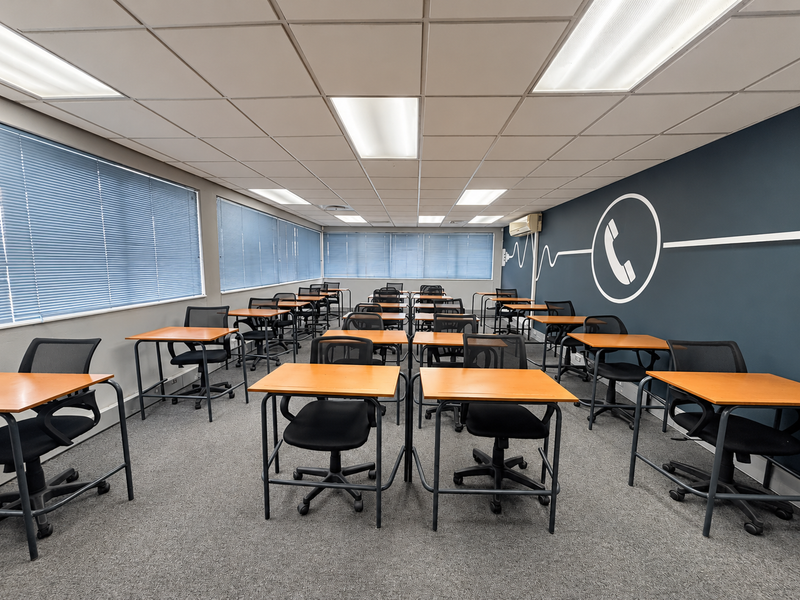 A functional office space featuring a suspended ceiling with recessed lighting, carpeted flooring, and large windows equipped with venetian blinds.
