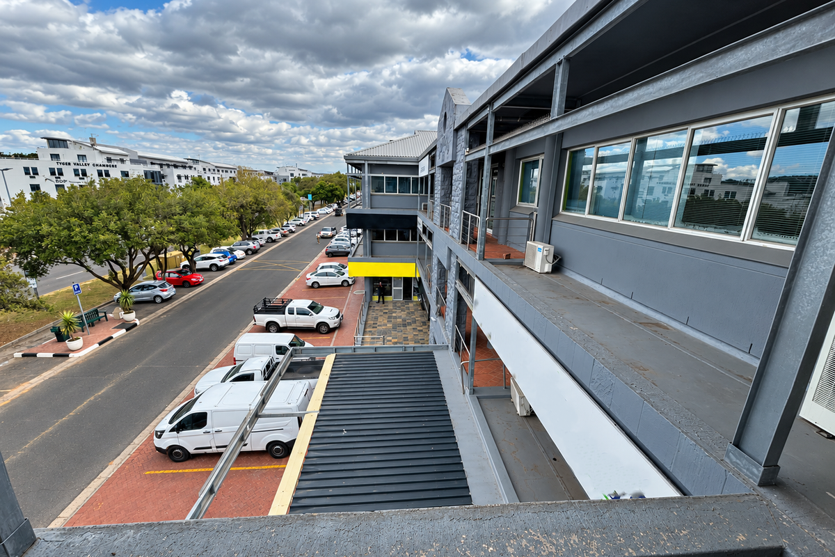 An elevated view of the office building exterior, featuring a balcony, large windows, and an external staircase overlooking the parking area.