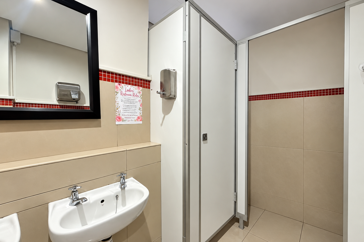 A clean and functional office bathroom featuring a wall-mounted basin, chrome fixtures, and a private toilet cubicle with neutral tiled finishes.