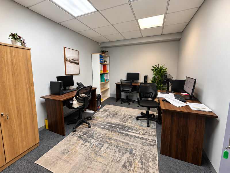 A functional office space featuring a suspended ceiling with recessed lighting, carpeted flooring, and a built-in storage cabinet.