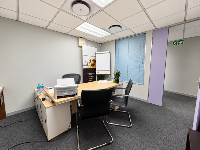 A functional office space featuring a suspended ceiling with recessed lighting, air conditioning vents, carpeted flooring, and large windows with venetian blinds.
