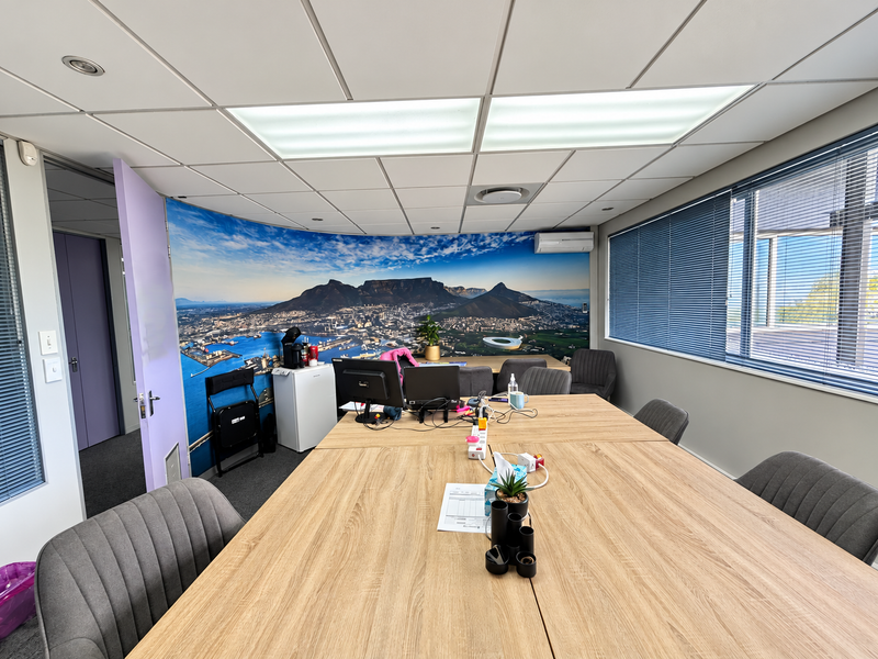 A functional office space featuring a suspended ceiling, recessed lighting, air conditioning, and large windows with venetian blinds, suitable for professional use.