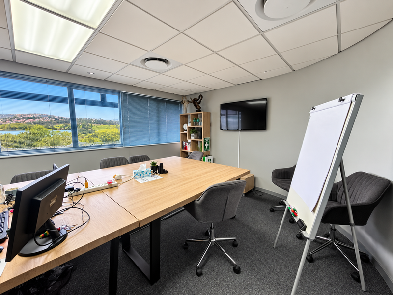 A professional office meeting room featuring a large conference table, carpeted flooring, suspended ceiling, and expansive windows with scenic views.