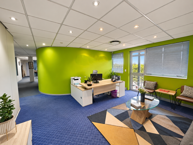 A bright, modern office space featuring a curved accent wall, suspended ceiling with recessed lighting, and large windows with venetian blinds.