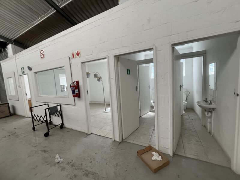 Industrial utility space featuring multiple partitioned rooms, including bathroom facilities with fixed sanitary ware and exposed structural ceiling elements.