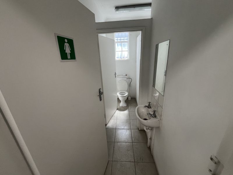A functional industrial-style restroom featuring a wall-mounted basin and a private toilet cubicle with tiled flooring and basic lighting.