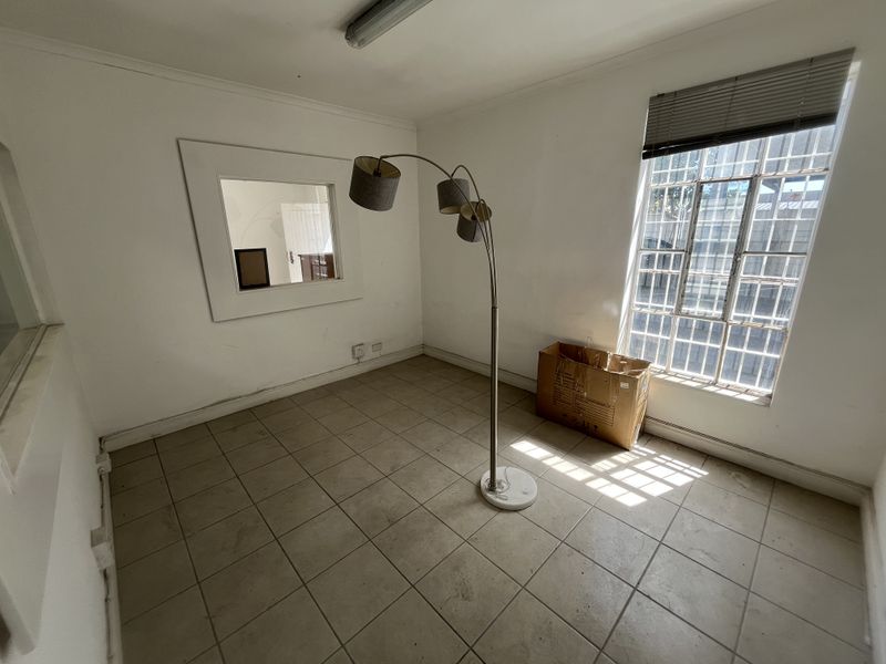 A vacant office space featuring tiled flooring, an internal window, and security bars on the exterior window, suitable for a professional workspace.