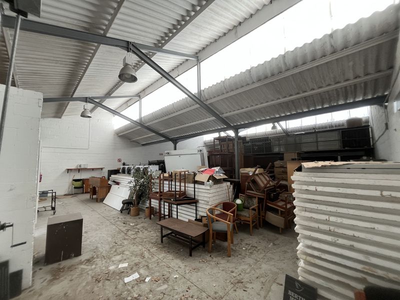 Spacious industrial utility area featuring exposed steel trusses, corrugated roofing with skylights, and durable concrete flooring, suitable for storage or workshop use.
