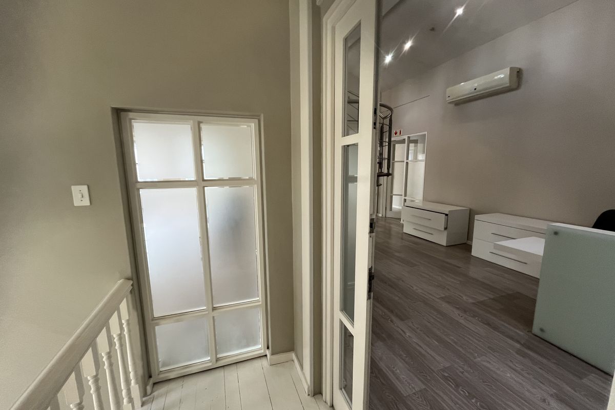A bright office space featuring laminate flooring, recessed lighting, a wall-mounted air conditioning unit, and a stylish internal glass door.