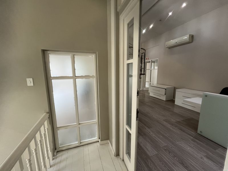 A bright office space featuring laminate flooring, recessed lighting, a wall-mounted air conditioning unit, and a stylish internal glass door.